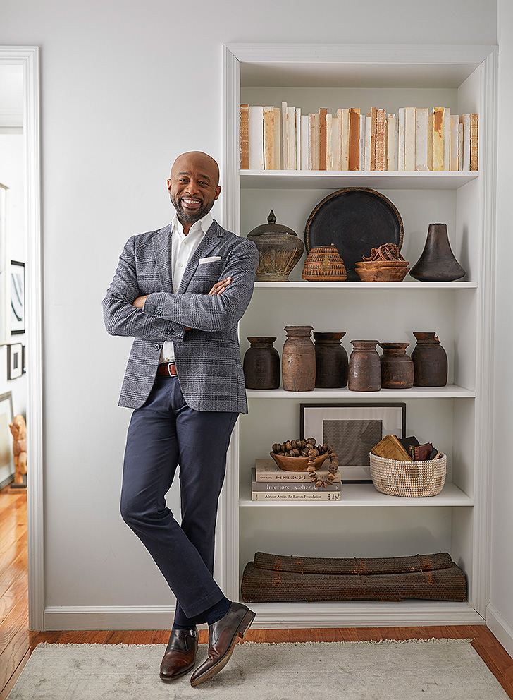 Designer Mikel Welch stands against a bookcase